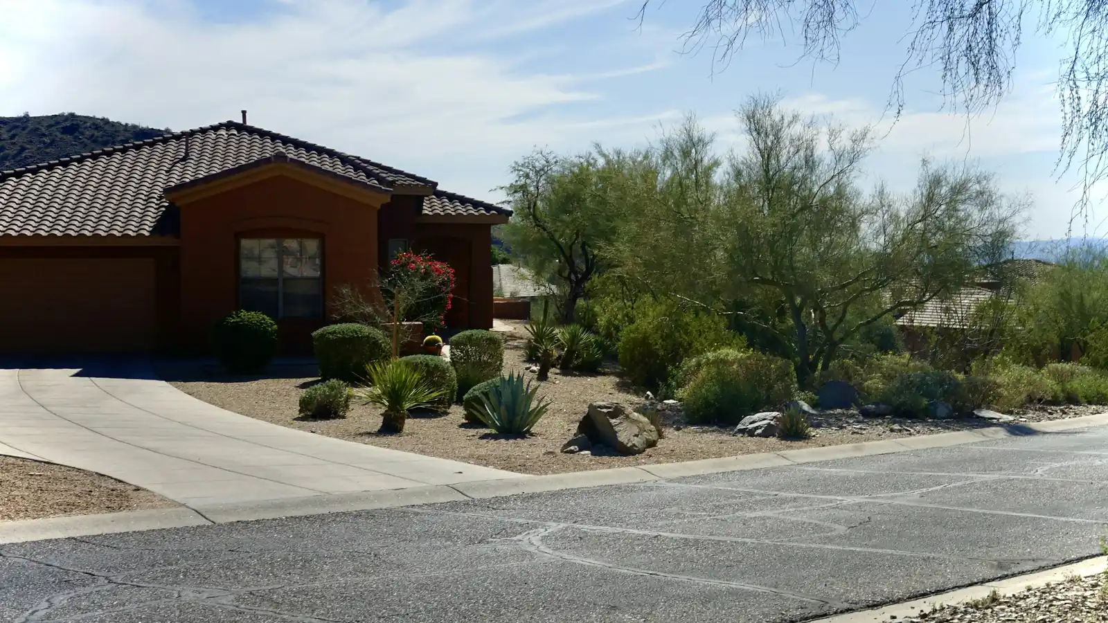 Single-story stucco home with a tile roof, a curved concrete driveway and a desert-landscaped front yard under a clear sky