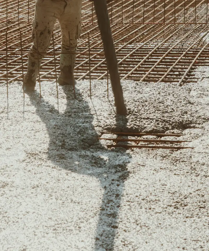 Concrete being placed over a grid of steel rebar while a worker in boots guides the pour