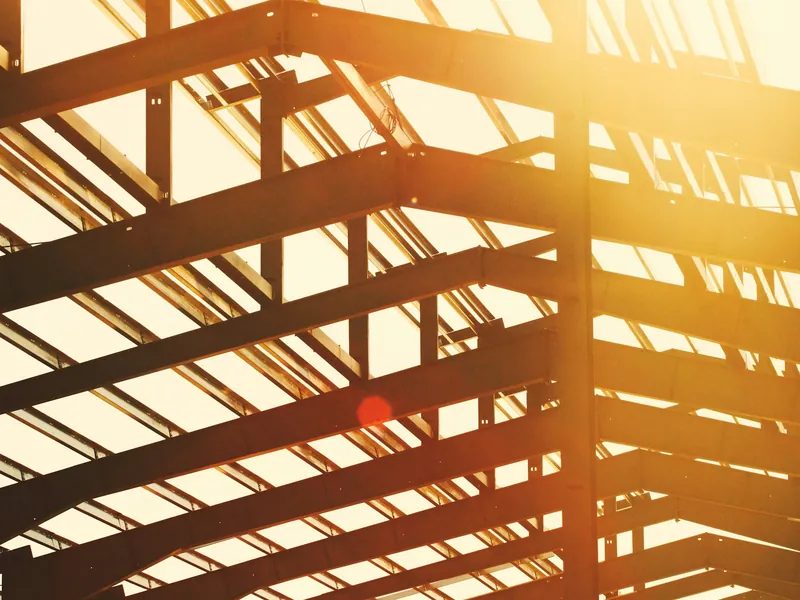 Steel roof trusses and purlins of a metal building frame lit by low afternoon sun