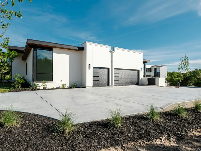 Wide new concrete driveway leading to a two-car garage, with fresh landscaping beds along the edge
