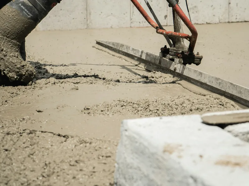 Power screed being pulled across freshly placed concrete beside a formed edge
