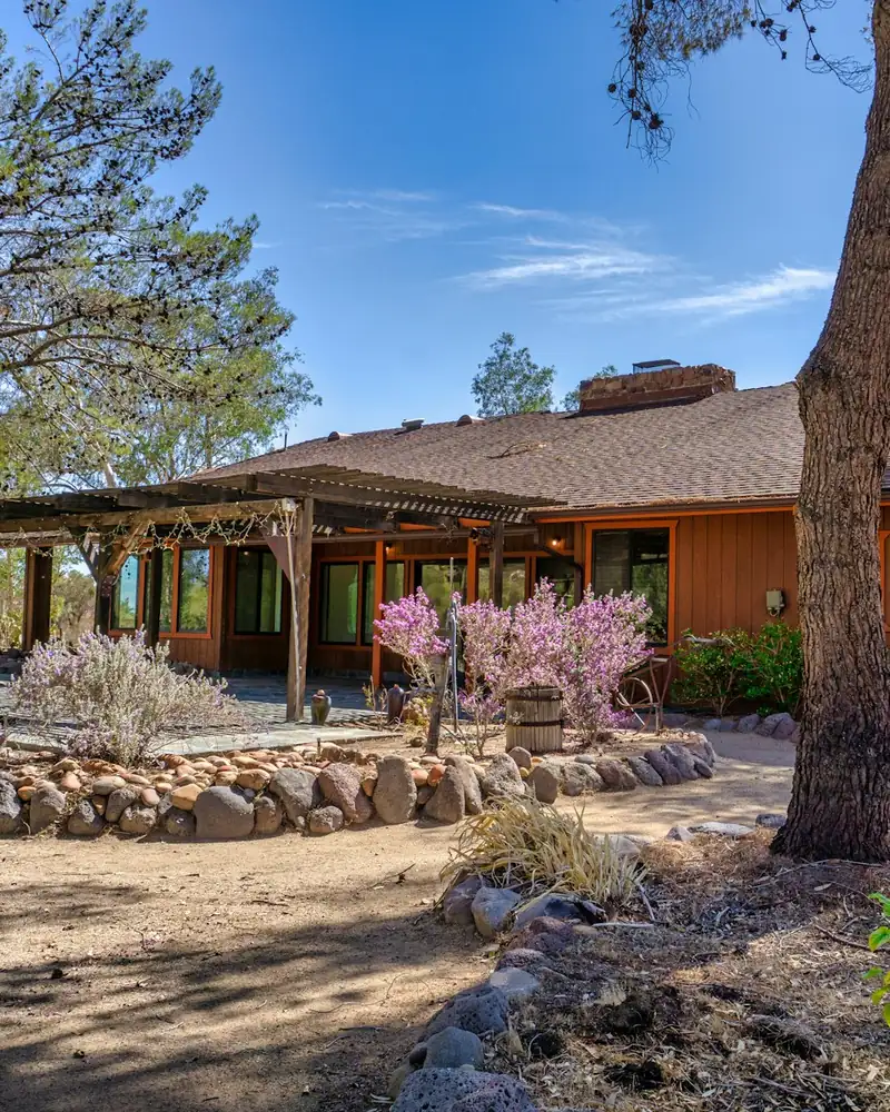 Ranch-style home with a covered porch behind a rock-edged garden and tall pines