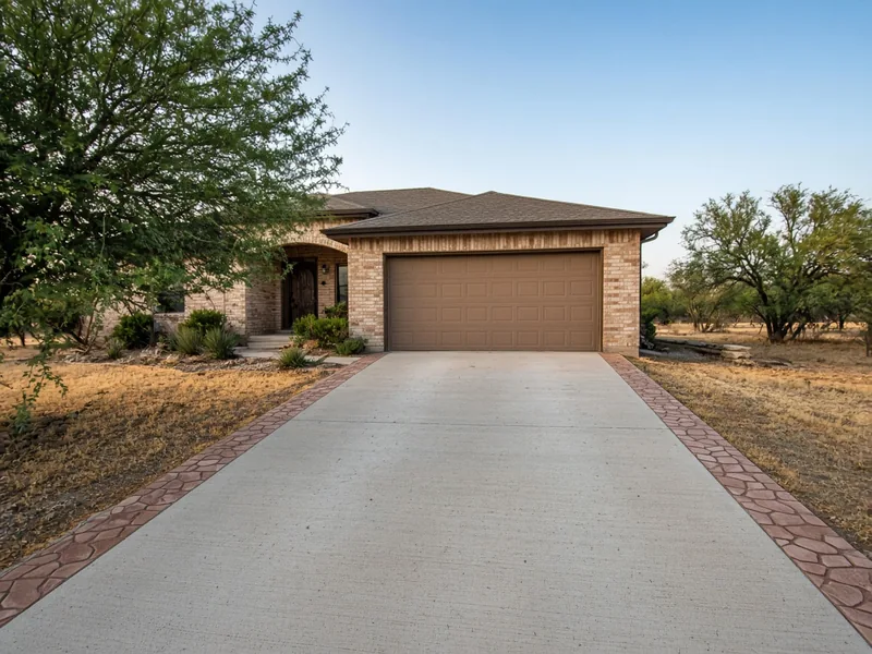 Broom-finish driveway framed by stamped cobblestone border bands at a brick ranch home